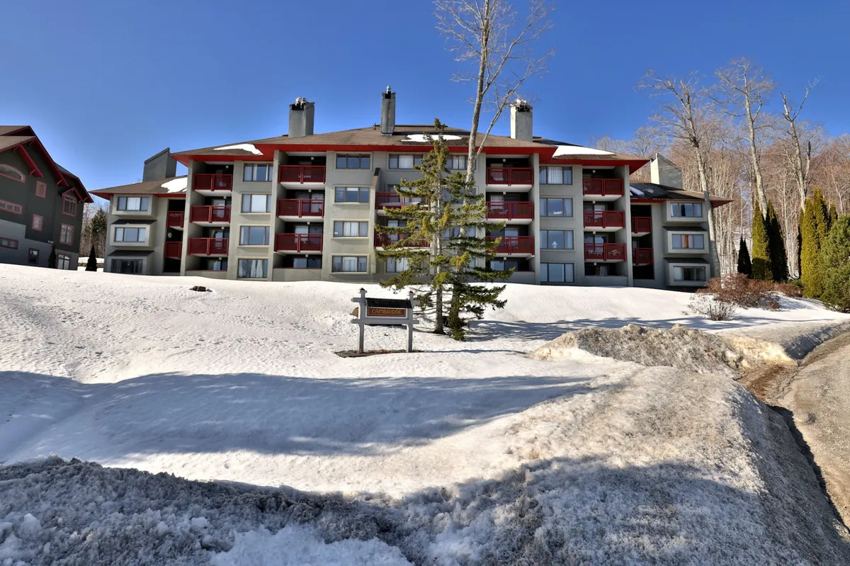 A cozy exterior image of a snow-covered building surrounded by tranquil winter scenery, with skiers and snowboarders seen enjoying the landscape. The scene evokes the inviting atmosphere of a winter haven, perfect for both adventure and relaxation.