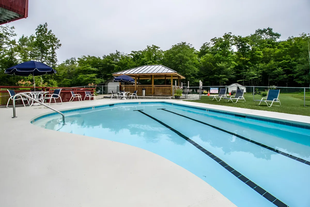 This exterior image highlights a sparkling swimming pool surrounded by lawn chairs and umbrellas, with a gazebo in the background. The tranquil setting is perfect for both swimming and lounging, and the area is large enough to accommodate families and groups. People can be seen enjoying the pool and outdoor space, making it ideal for social gatherings and barbecues.