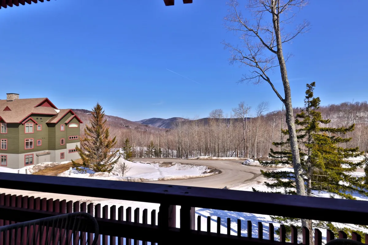 This image captures a tranquil view of mountains in the distance, a snow-covered ground, a green and red building, and surrounding trees. The scene radiates a sense of accessible adventure and natural beauty, with the possibility of hiking or relaxing outdoors in every season.