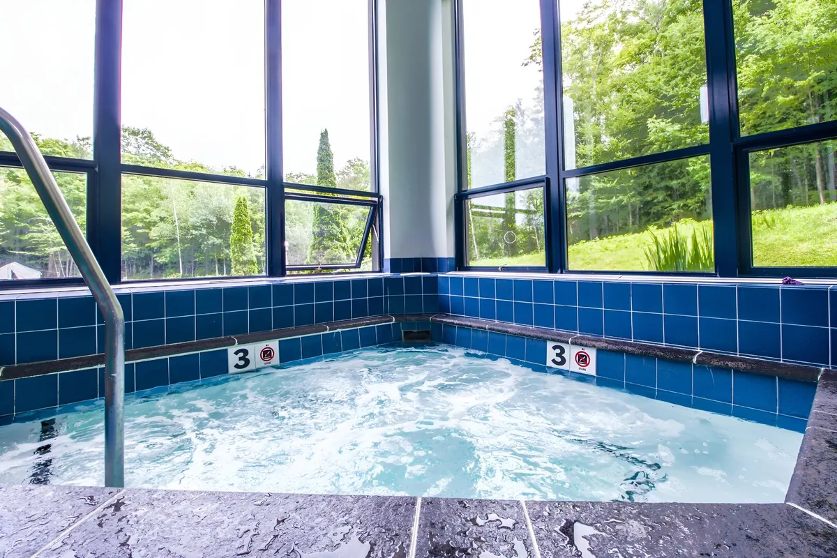 An inviting indoor scene at the Sunrise Sports Center featuring a bubbling hot tub, large windows with natural views, and tranquil lighting. The space exudes relaxation and comfort after a day in the snow.