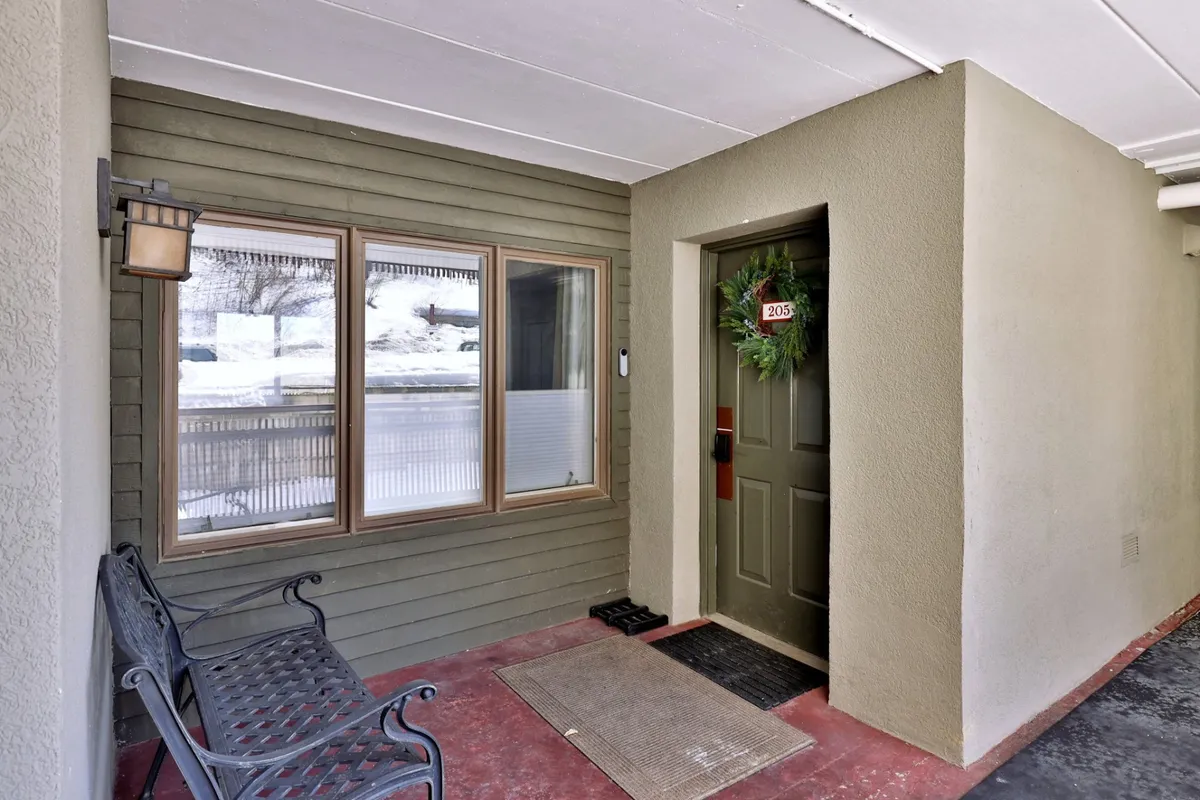 A welcoming view of the property’s front door, adorned with a wreath, a cozy bench, and large windows. The scene suggests easy access, a warm welcome, and a connection to the natural setting just beyond.