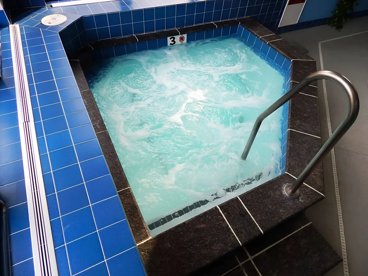 A peaceful indoor hot tub area with soothing tile patterns and clear, inviting water. The handrail and cozy surroundings suggest a focus on comfort and relaxation, ideal for unwinding after a day of activities. The setting is intimate, suitable for couples or individuals seeking a spa-like experience.